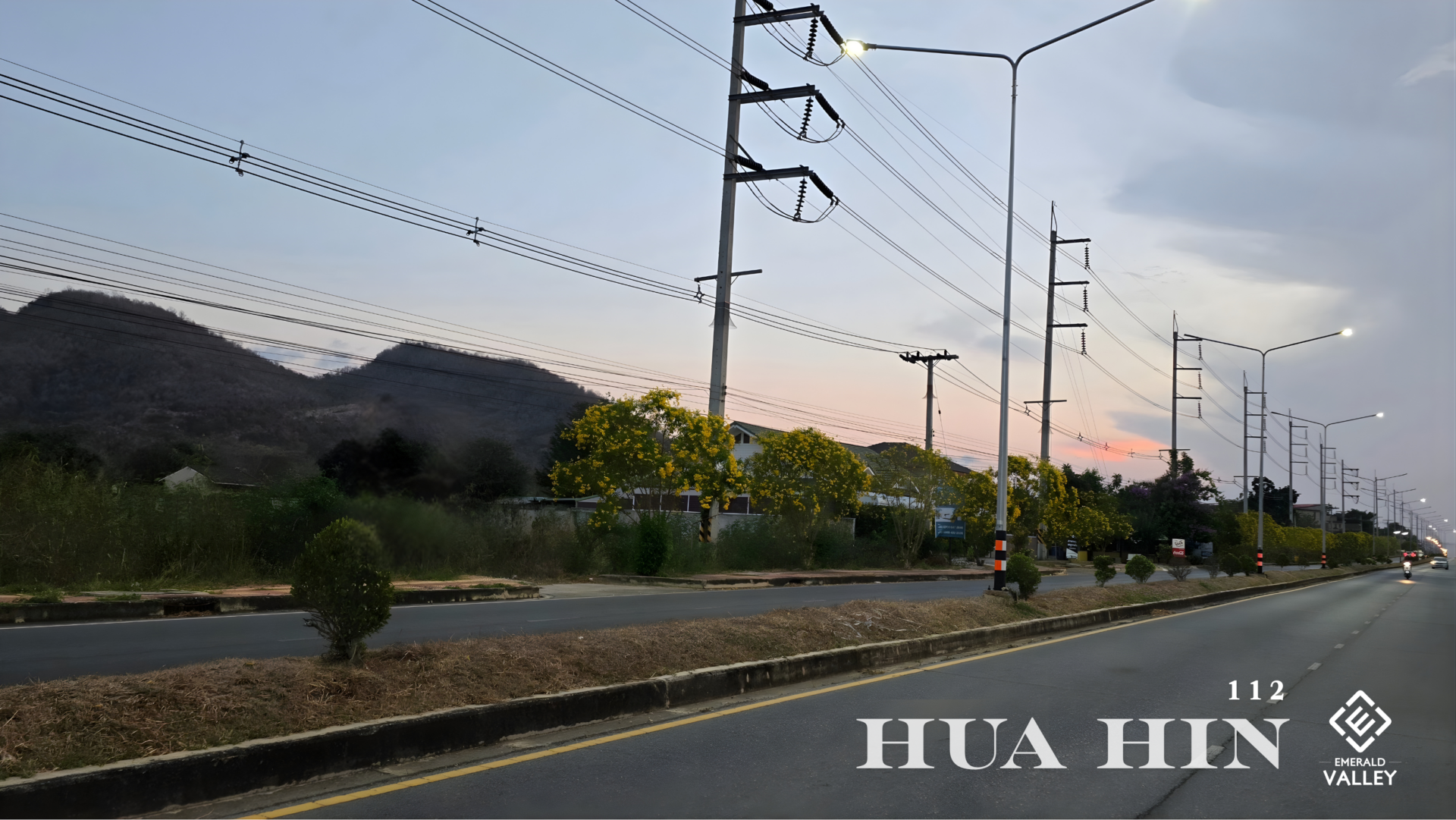Scenic mountain view along the Hua Hin 112 road near Emerald Valley Hua Hin featuring vibrant yellow flowering trees at sunset.